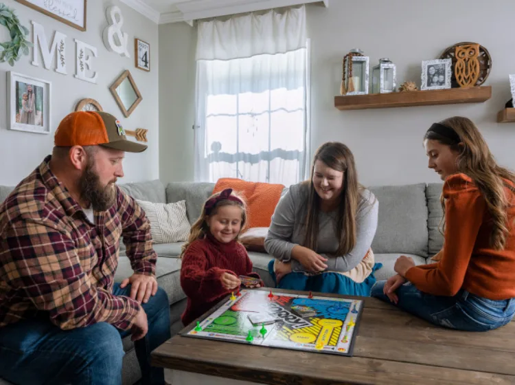 A father, mother and two daughters sit on a couch and play a board game in their Clayton home.