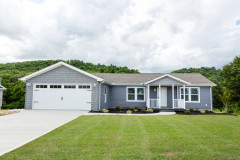 Manufactured home exterior with blue gray siding, white trim around the windows and doors, a small porch, and a matching attached garage, with a concrete driveway and a green lawn.