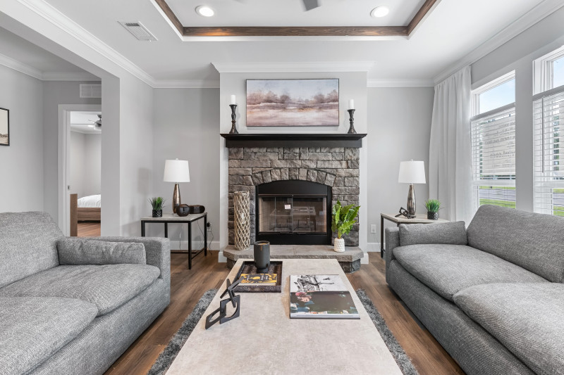 Living room of a Clayton manufactured home with gray walls and couches, wood floor and a stone fireplace with a mantel