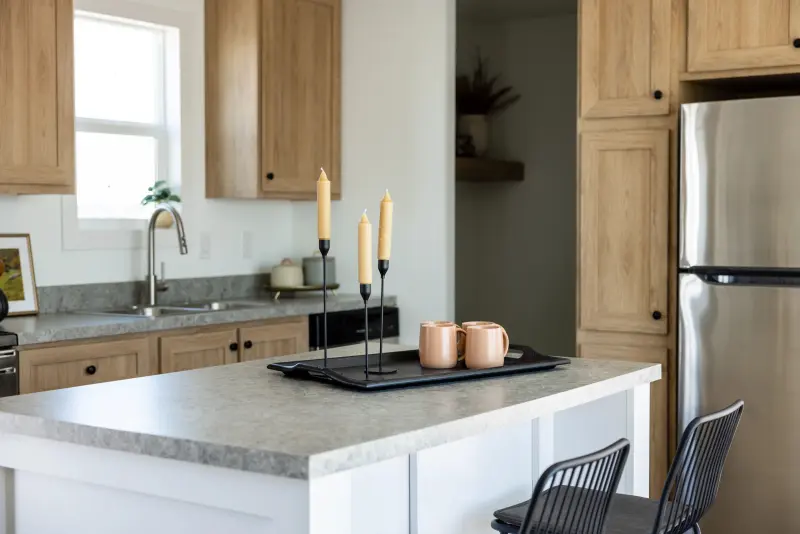 Manufactured kitchen with a white island in the middle with black design elements and light wood cabinetry. 