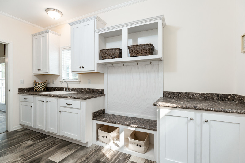 Laundry room in the 1714 Heritage manufactured home that features a mud room bench, sink and lots of white cabinets.