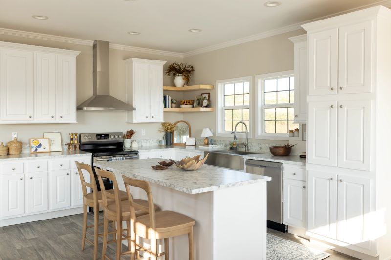 Clayton manufactured home kitchen with white cabinets, stainless steel appliances and an island with three chairs, along with neutral decor.