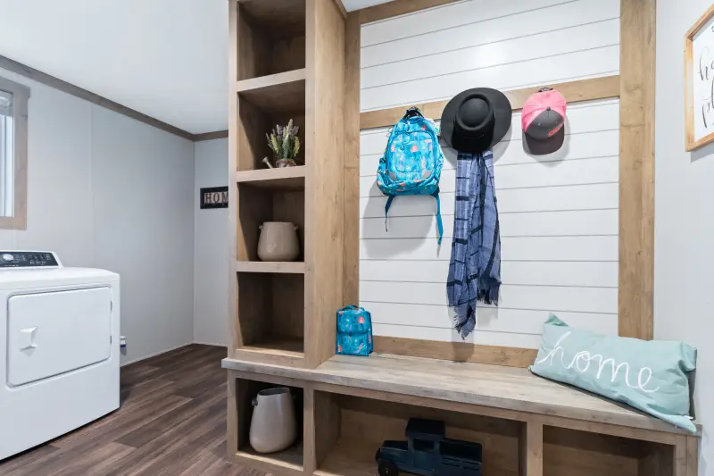 A laundry room with a built-in bench and hooks holding a backpack and hats.