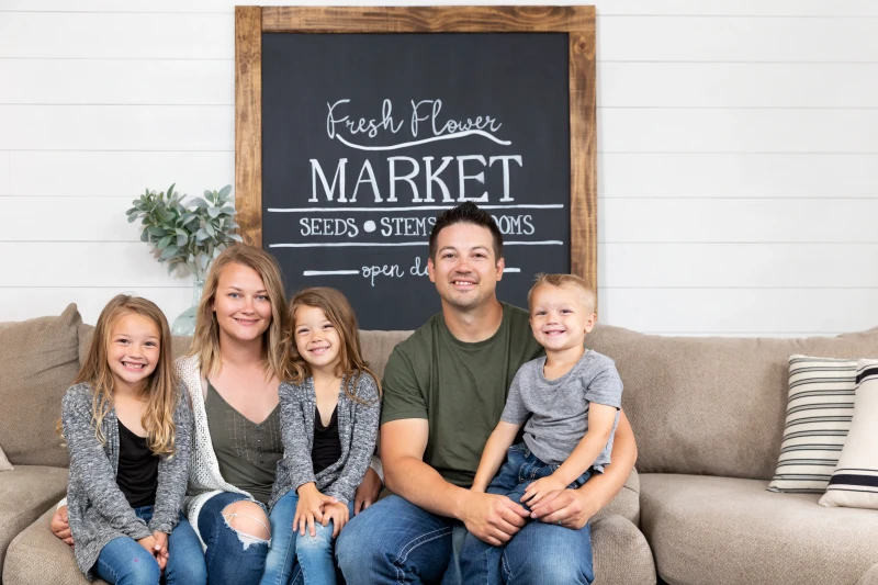 Family sits on couch in farmhouse living room in front of a shiplap wall. 