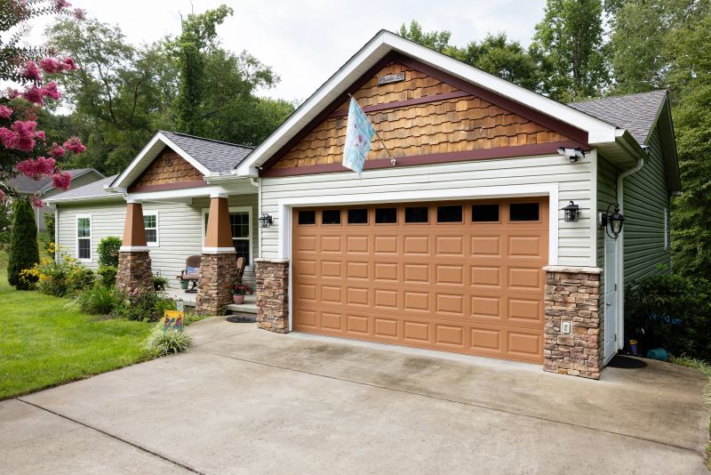 Exterior of a modular home with light green siding, brown trim and stone and wood accents, with a porch.