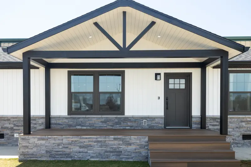 Exterior of Clayton manufactured home with cream siding, dark trim and a dark wood front porch with stone skirting