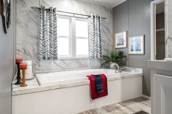 The primary bathroom of [model name] features an alcove tub and a marble-style accent wall.