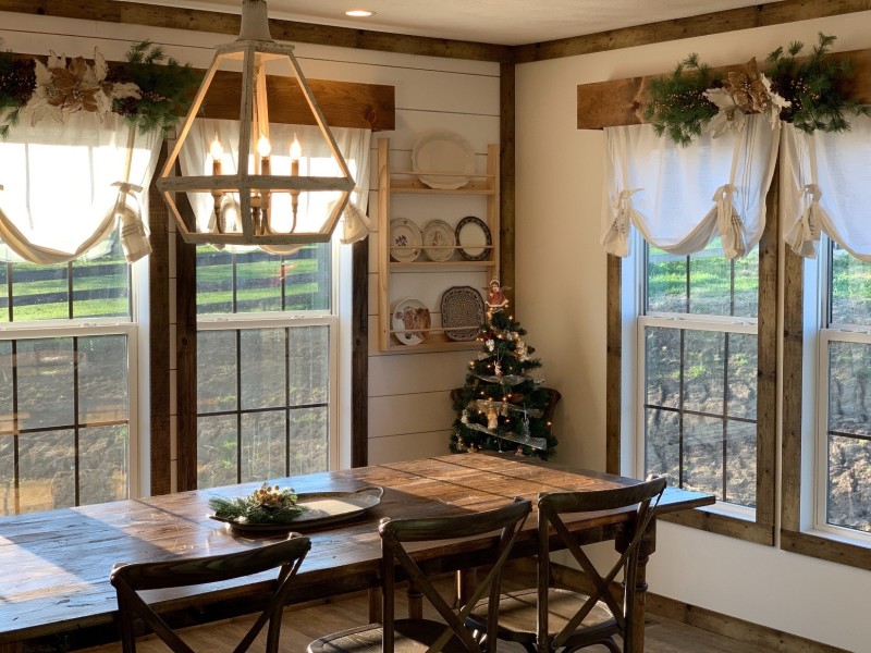 Dining room with wooden table, wooden chairs, large windows and farmhouse decor.
