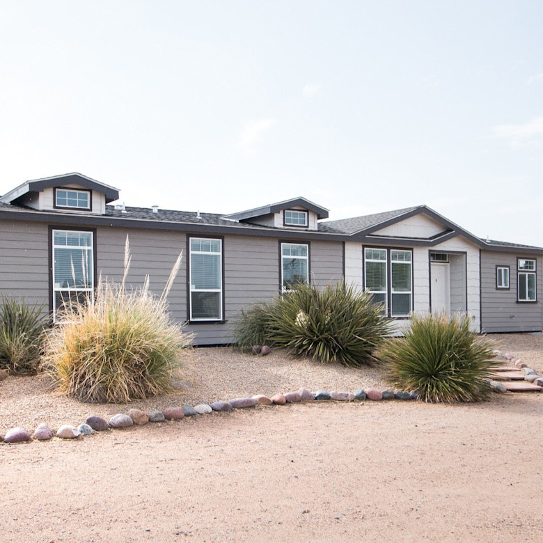 Exterior view of a manufactured home with desert landscaping.
