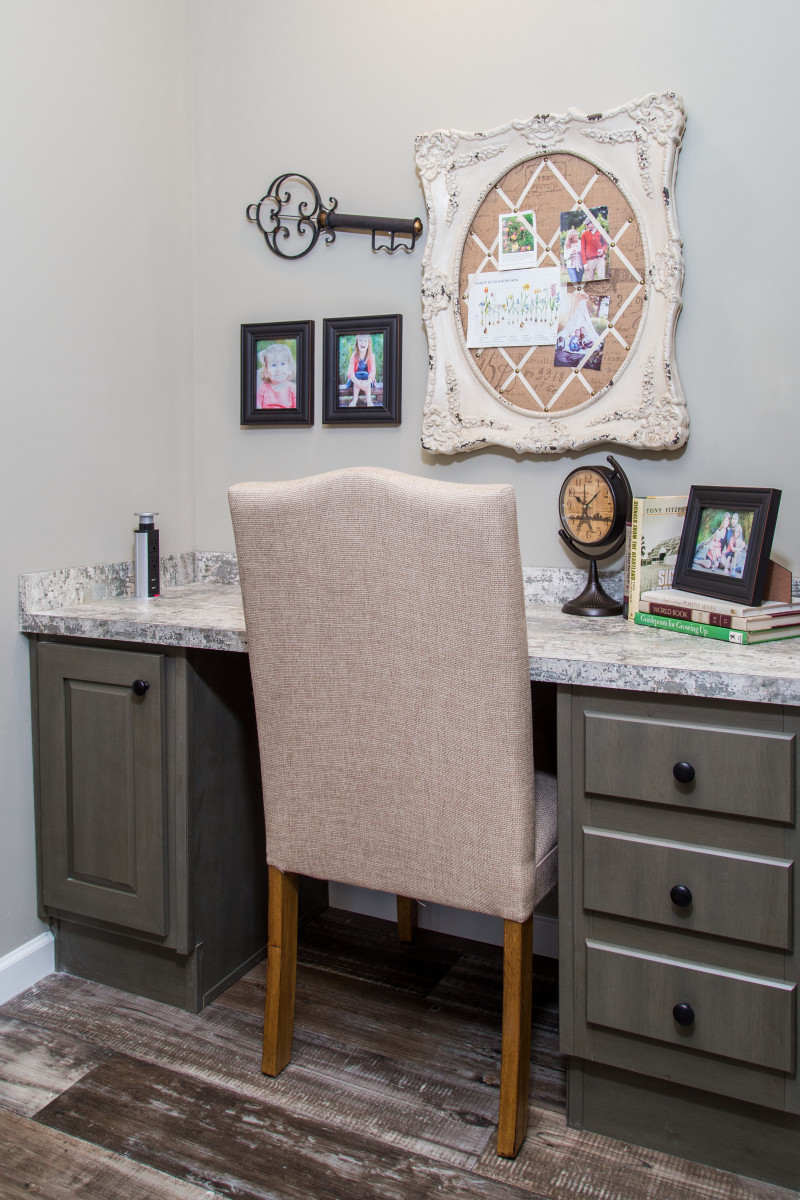 There’s a small, decorated office nook with brownish green built-in drawers and a white chair pulled into the desk area.