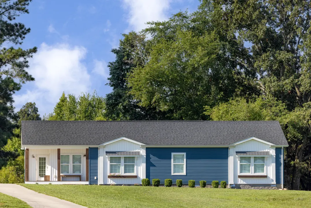 Blue and white exterior of the Southern Charm Clayton Model with green grass, landscaping, and a spring day in the background. 