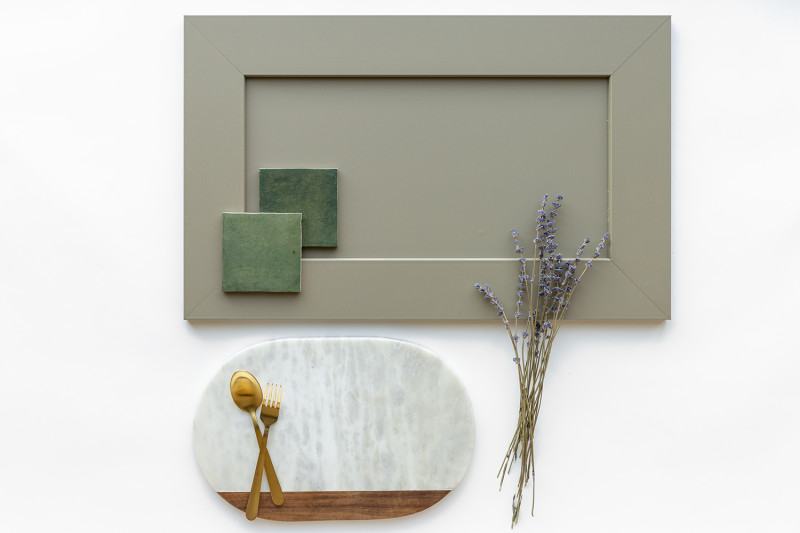 A flat lay with a sage green cabinet, lavender plant, green tiles and a marble and wood cutting board