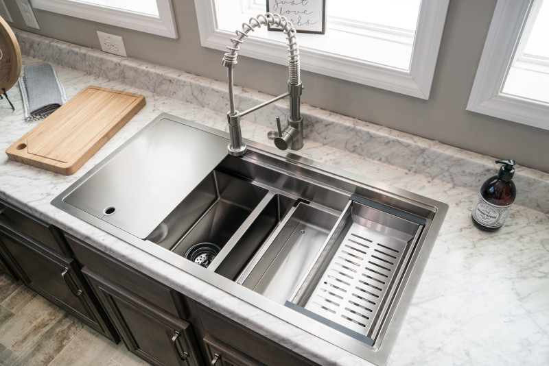 A modern stainless steel kitchen sink with different components like a cover and drying rack.