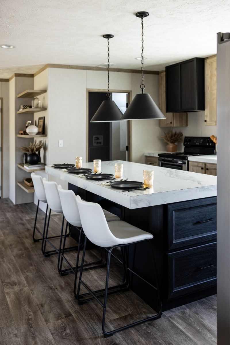 Kitchen with black kitchen island and cabinetry. Island has white countertop and white high top chairs pulled up to it.