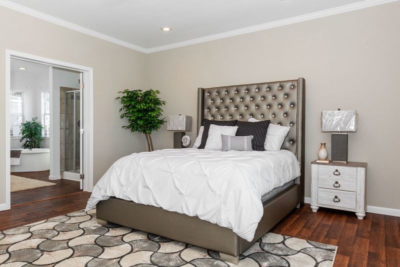 Primary bedroom with a bed, side tables and a large patterned rug. Room is beige styled with white and brown tones.