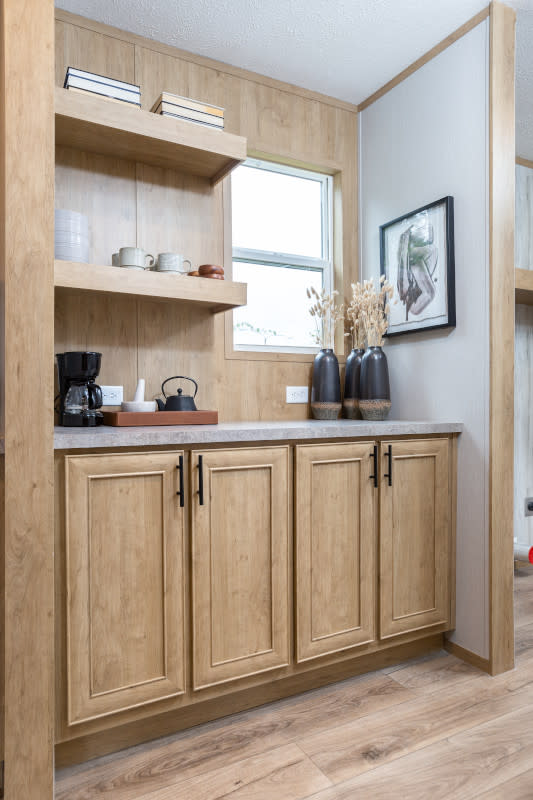 Small coffee nook with honey-colored cabinets, a small window and two shelves. Countertop is filled with coffee pot and coffee accessories.