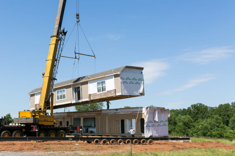 Crane setting up double-wide modular home at a home site.