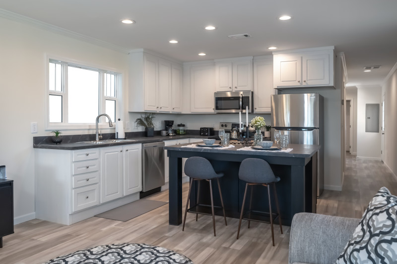 An L-shaped kitchen with white cabinets, stainless steel appliances, and a dark, square shaped island set for two.