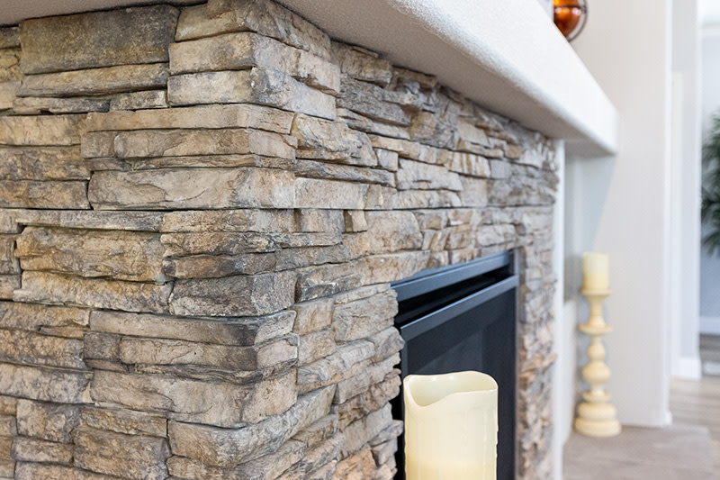 Closeup of light brown and gray stone fireplace with white mantel and 2 cream candles on the hearth.