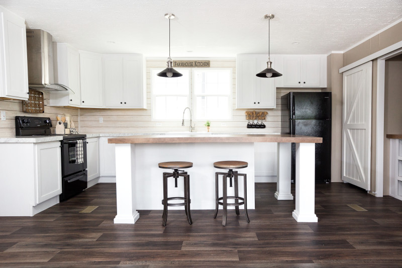 A farmhouse kitchen in a manufactured home with shiplap walls, a kitchen island and white cabinets.