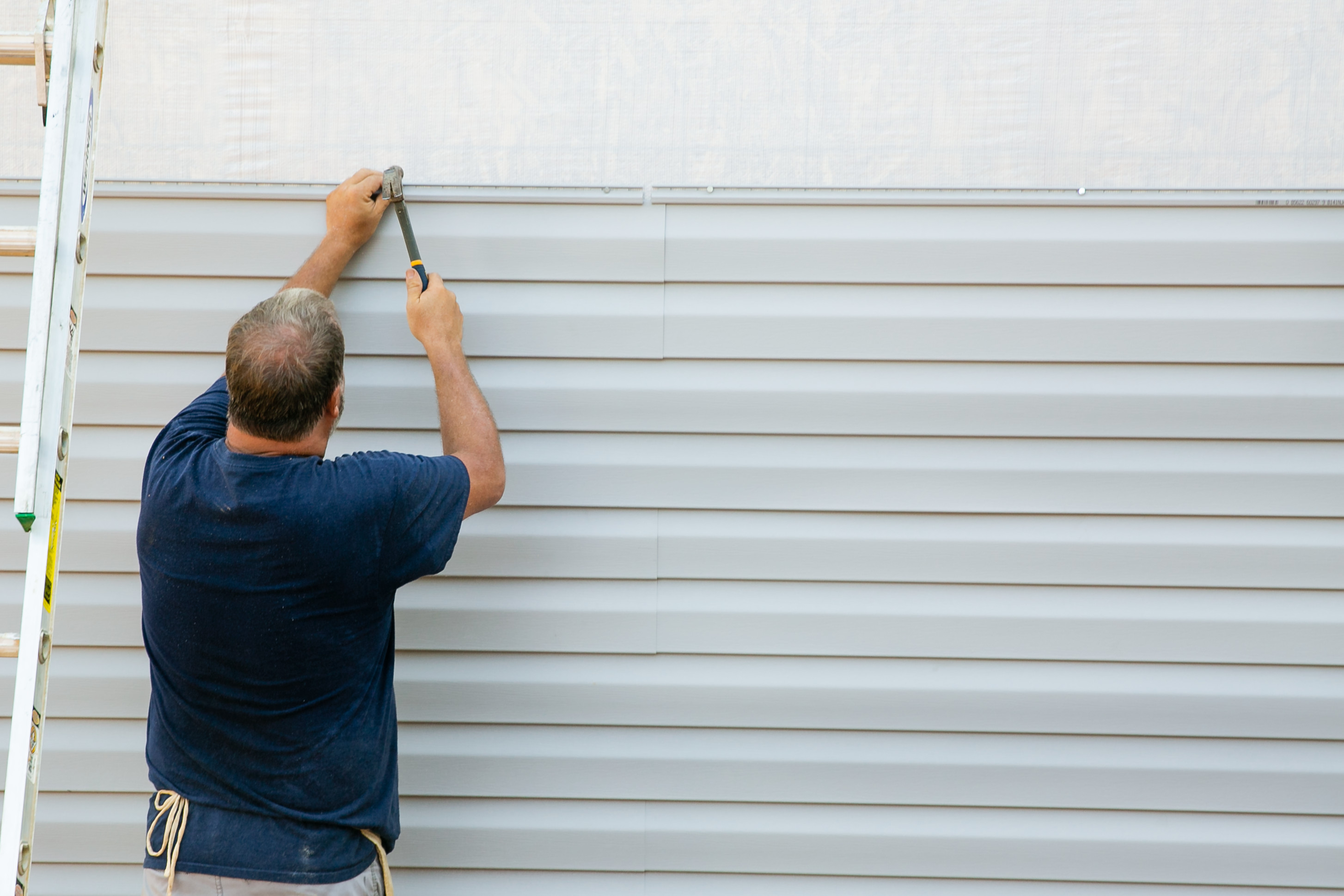 Man hammering a nail into the siding of a manufactured home.