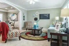 View of the interior of a manufactured home with the living room and part of the kitchen in view. Rooms are bright with light and decorated with lots of color.