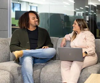 Two Clayton team members sit on a gray couch facing each other.