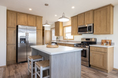 Kitchen of a Clayton manufactured home with light wood cabinets, stainless steel appliances, light wood floors and a white and gray island with two stools
