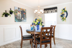 Dining room of a Clayton Built® manufactured home featuring white wainscoting, blue, green and yellow decor and a dark wood table with 4 matching chairs.