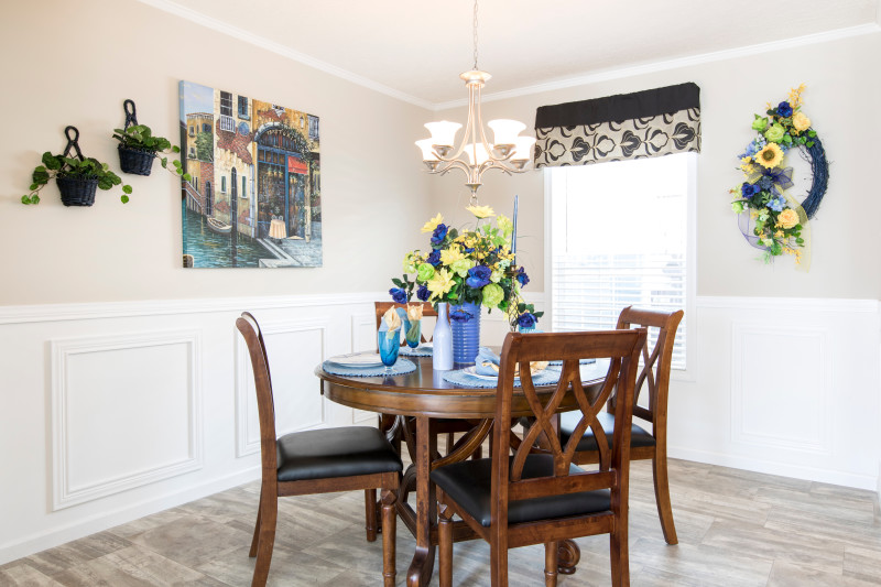 Dining room of a Clayton Built® manufactured home featuring white wainscoting, blue, green and yellow decor and a dark wood table with 4 matching chairs.