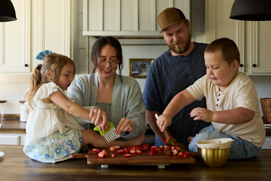 The Isaacks family cuts strawberries together in the kitchen.