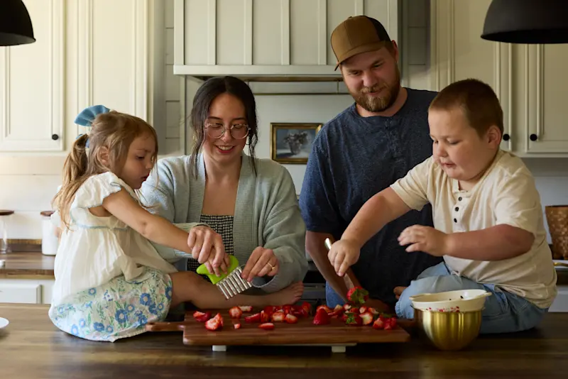The Isaacks family cuts strawberries together in the kitchen.