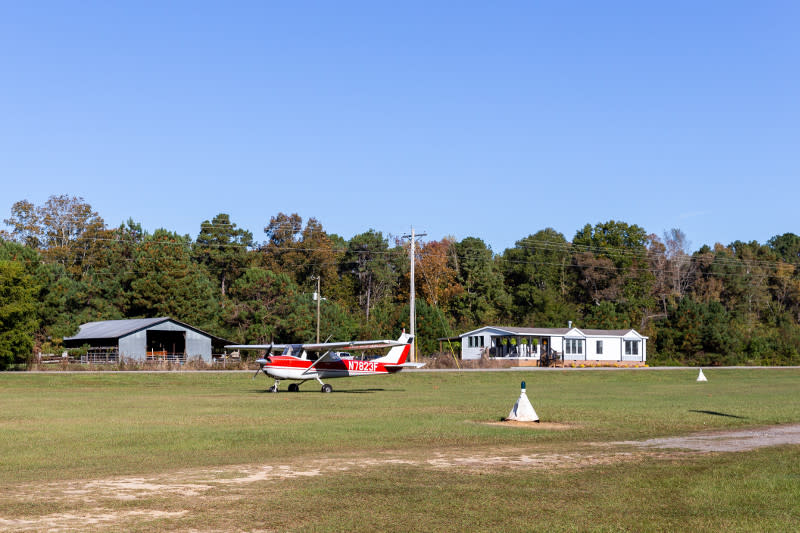 Red airplane on runway in front of manufactured home.