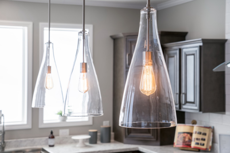 Warm old-style bulbs hang in a kitchen. They have fluted glass coverings over them that allow you to still see the bulb design.