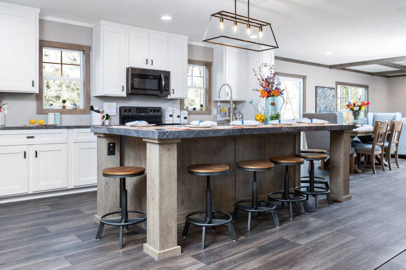 Kitchen of a Clayton manufactured home with white cabinets, a large island and wood style floors, with a dining room in the background.