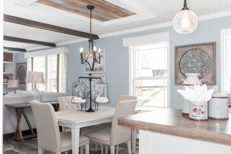 Dining room of a Clayton manufactured home with a tray ceiling and window cornices, with the living room on one side and the kitchen island on the other