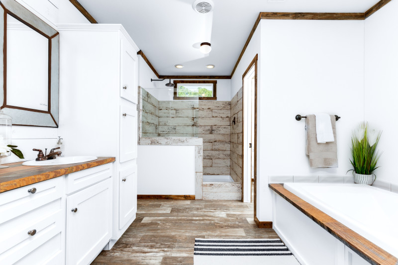 A large bathroom in a manufactured home with a walk-in shower, separate bathtub and white cabinetry.