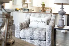 Gray toned chair with white pillow that says ‘let’s stay home’ in gray lettering.