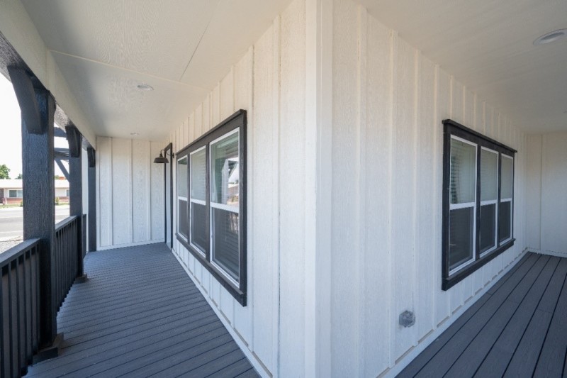 Exterior of home with wrap porch. Manufactured home is white with dark brown decking. 