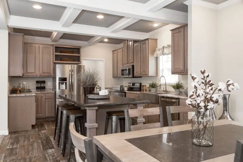 A manufactured home kitchen and dining area with wood styled cabinetry and a large breakfast bar. 