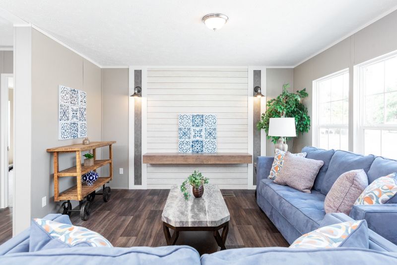 There’s a white living room with natural light coming in though the windows and a white and gray shiplap focal wall lines the back wall. There are blue couches and a coffee table. 