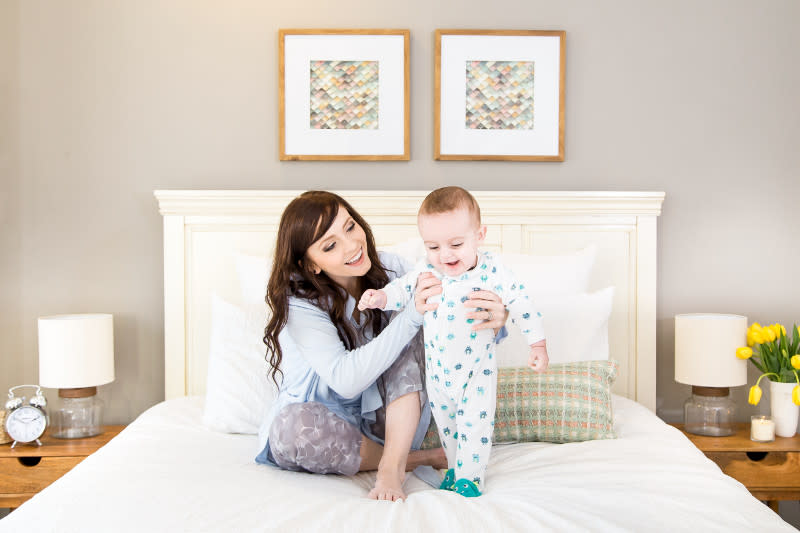 A young mom sitting on her bed and playing with her smiling baby.