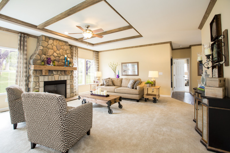 There's a living room with light yellow walls, a wooden beam tray ceiling, and a huge stone fireplace. It's filled with neutral colored furniture.