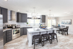A kitchen in a manufactured home with a white kitchen island with stools, gray cabinets and an adjacent eating area.