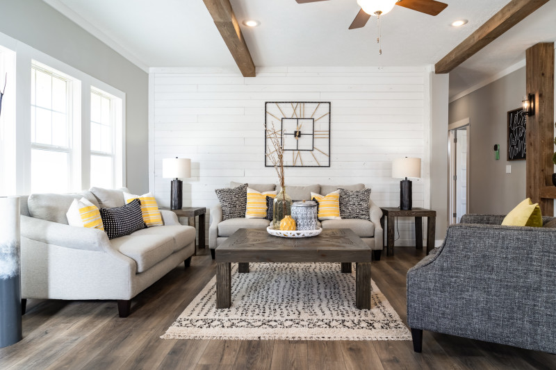Manufactured home with shiplap accent walls, wood ceiling beams, and cloth couches with decorative pillows
