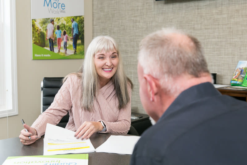Woman with gray hair and pink sweater smiles at camera as she signs paperwork at a home center.