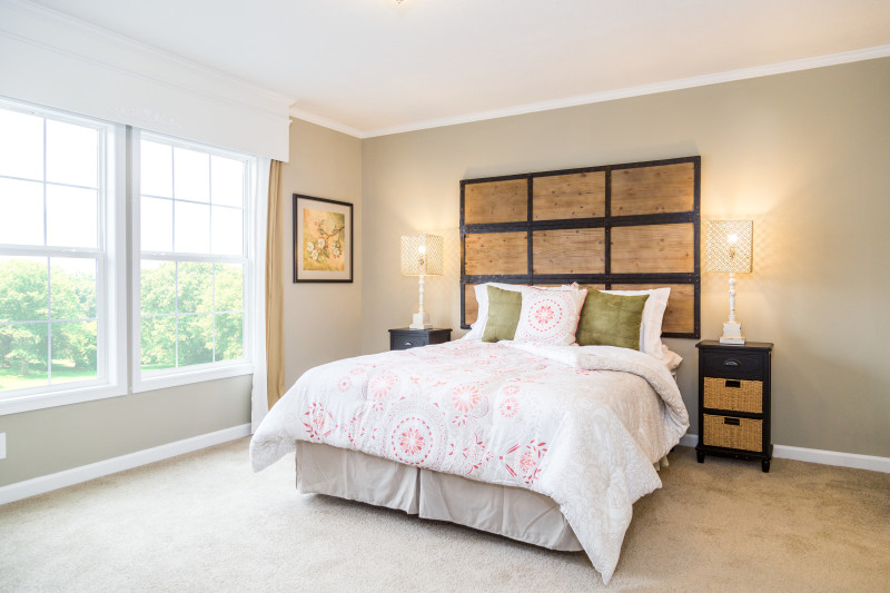 A primary bedroom is in view with tan walls and light coming through the window. There’s a bed with a large wooden headboard.