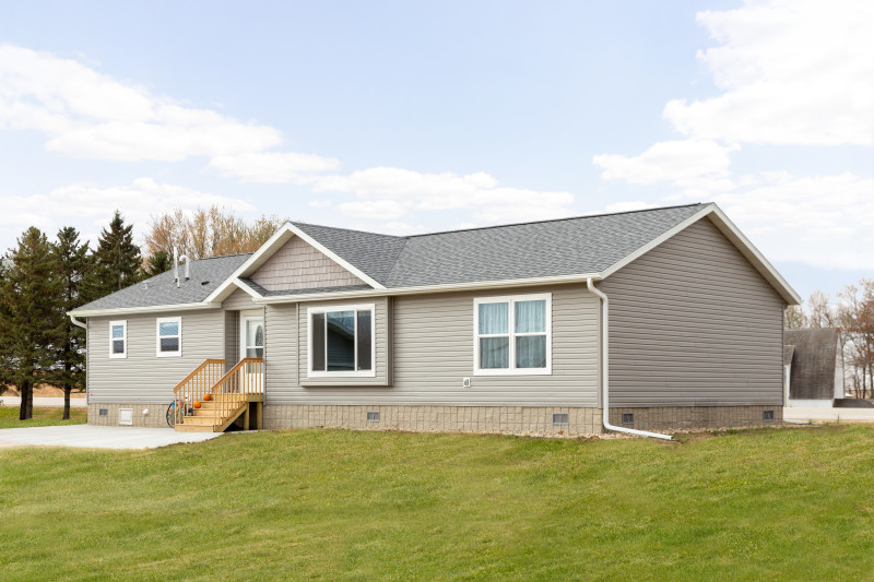 Exterior of a manufactured home with light tan siding, gray roof, white trim and stairs, with a driveway and grass in front.