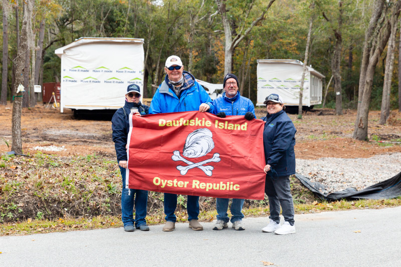Stefanie, Norbert, Ted and Pam holding a red Oyster Republic flag in front of the delivered Clayton homes.