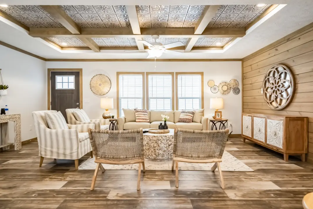 A living room with a tin tray ceiling with wood ceiling beams, a wood paneled wall on the right and wicker and neutral upholstered furniture around a small round coffee table.